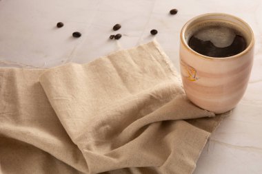 Önünde bej peçete olan mermer bir arka planda kahve fincanı.