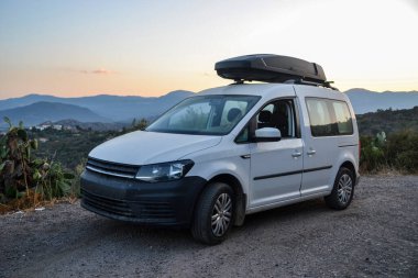 Sardinya 'da yaz tatili: Tozlu bir yolda park edilmiş çatı kutusu olan, engebeli dağlarla çevrili ve yaz macerasının ruhunu yakalayan daha büyük bir araç..