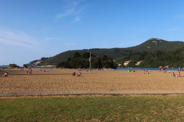 İspanya 'nın Bask Bölgesi' ndeki San Antonio Sahili 'nde kumlu bir sahil, sakin bir deniz ve açık bir öğle vakti mavi gökyüzü ile yakalanan uzak yeşil dağ zirveleri bulunur.