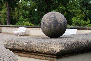 Prag Kraliyet Bahçesi 'nde tarihi bir Plinth üzerinde yıpranmış taş küre ve arka planda banklar ve yeşillik