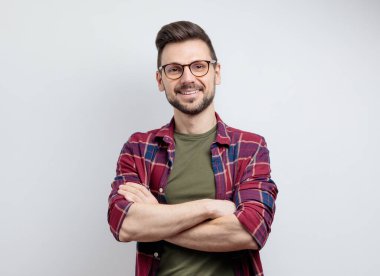 Sıradan gömlekli yakışıklı genç adam kollarını kavuşturup gülümsüyor. Gri arkaplan