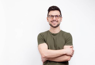 Gözlüklü, sıradan tişörtlü, mutlu yüzlü, kollarını kavuşturup kameraya bakan genç bir adam.