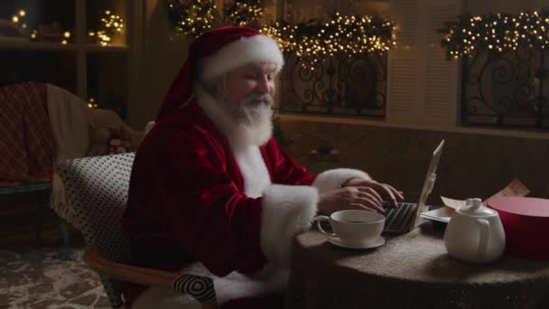忙碌的圣诞老人深夜在他的家里工作 在笔记本电脑上打字 做笔记和计划 喝热茶 慢动作 — 图库视频影像