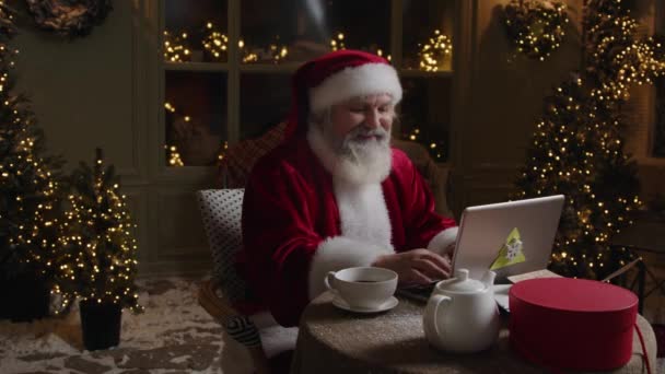忙碌的圣诞老人在他的家里用笔记本电脑工作 做着一些笔记和计划 开心地微笑着 享受着节日前的时光 慢动作 — 图库视频影像