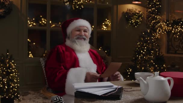 圣诞老人 白胡子老人 坐在桌旁 对着摄像机笑着 读着一封信 寒假季节 慢动作 — 图库视频影像