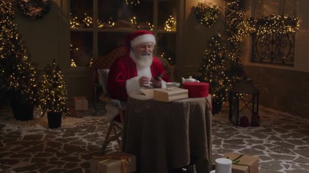 Zajęty Święty Mikołaj Siedzi Podwórku Rozmawia Przez Telefon Komórkowy Przygotowuje — Wideo stockowe