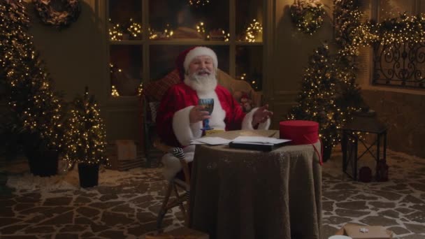 圣诞老人坐在后院 看着摄像机 一边聊天 一边祝寒假愉快 一边举杯 冬天祝贺 慢动作 — 图库视频影像