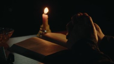 Yumuşak mum ışığında bir masanın üzerinde açılmış İncil kitabı, dua kutsal kitabı, ruhani uygulamayı, yüksek kaliteli 4K görüntüleri okumaktır.