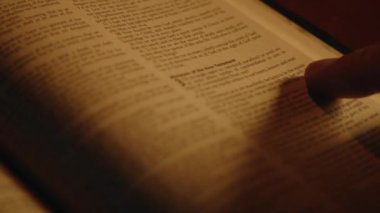 İnananlardan biri İncil 'i okuyor, kutsal kitap bir masanın üzerinde, yumuşak mum ışığında, ruhani pratikte, yakın çekim, yüksek kalite 4K görüntü.