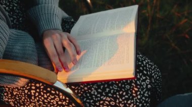 Kadın sandalyede oturuyor ve kitap okuyor, hobisinin keyfini çıkarıyor, açık havada, yakın çekim, yüksek kalite 4K görüntü.