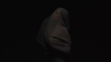 Çarpıcı bir karanlık arkaplana karşı akışkan kumaşla örtülmüş bir figürün unutulmaz tasviri.