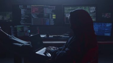 Kararlı bir hacker, loş bir odada, karmaşık kod gösteren sayısız ekranla çevrelenmiş bir şekilde derinden odaklanır.