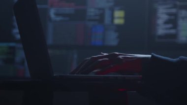 Siluetli eller dizüstü bilgisayarda yazmakla meşguller, loş ışıkla hafifçe aydınlatılmış, benzersiz bir teknoloji atmosferi çağrıştırıyor.