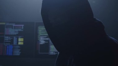 Bir kapüşonluyla örtülmüş gizemli ve gölgeli bir figür, dönen bilgisayar kodlarıyla çevrelenmiş, siber zekayı somutlaştırıyor.