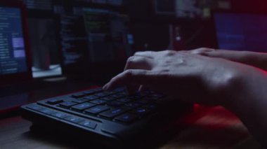 Klavye üzerinde ustalıkla çalışan eller koyu renk ortamda parlayan ekranlarla çevrilidir.