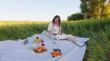 Lezzetli meyvelerin pikniği sırasında güzel bir çayırda büyüleyici bir kitap okumayı seven bir kadın.