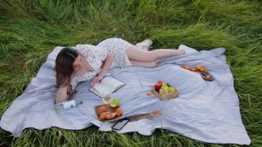 Bir kadın açık havada huzurlu bir piknik yapar, kitap okur ve etrafı taze meyve ve atıştırmalıklarla çevrilidir.