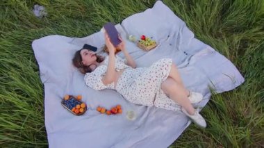 Huzurlu bir piknik sahnesi. Büyüleyici bir kitaba dalmış bir kadın. Etrafı yemyeşil bir tarlayla çevrili.