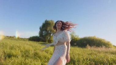 Neşeli genç bir kadın neşeli bir şekilde güneşli bir günün tadını çıkarıyor. Parlak ve canlı yeşil bir alanda, doğayla çevrili.