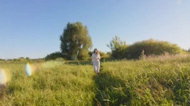 Genç bir kadın güneşli yeşil bir tarlada geziniyor, doğanın güzelliklerinin tadını çıkarıyor.