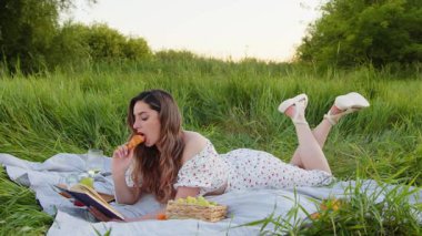 Genç bir kadın büyüleyici bir kitapla meşgul olurken doğa güzelliğindeki lezzetli atıştırmalıkların tadını çıkarıyor.