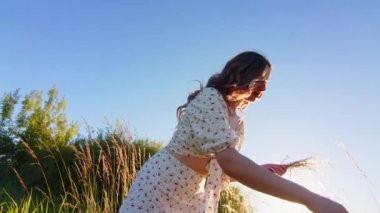 Neşeli bir kadın zarif bir şekilde yukarıdaki parlak ve güneşli gökyüzünün altındaki yemyeşil çimlerle etkileşime girer.