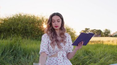 Genç bir kadın büyüleyici bir kitaptan ve dingin, hayat dolu bir çiçek tarlasında ferahlatıcı bir içecekten hoşlanır.