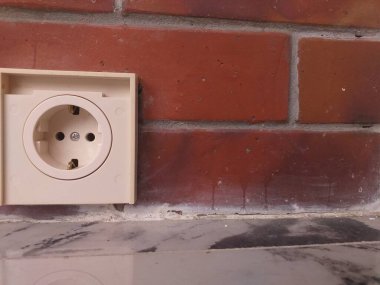 Beyaz elektrik prizi parlak kırmızı tuğla bir duvara monte edilmiş. Konut veya ticari ortamlarda elektrik tesislerinin resimlendirilmesi için ideal.