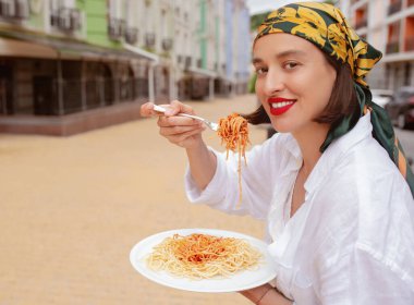 Sokakta spagetti yiyen genç bir kadın. Fast food konsepti, seyahat.
