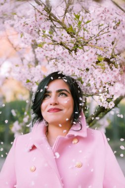 İlkbaharda kiraz çiçeklerinin altında pembe paltolu güzel bir kadının portresi.