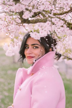 İlkbaharda kiraz çiçeklerinin altında pembe paltolu güzel bir kadının portresi.