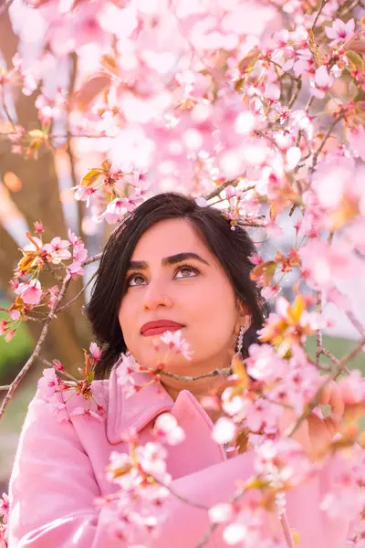 İlkbaharda kiraz çiçeklerinin altında pembe paltolu güzel bir kadının portresi.