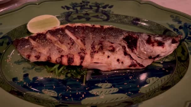 テーブルの上の皿の上に置かれた食べ物の近くに 高品質の4K映像を公開しました ブラックプレートで焼いた魚 グリルしたシーベース ライムとタイムでグリルしたシーベースのフィレット レストランでサービス おいしい — ストック動画