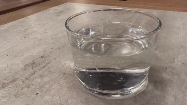 把杯子里的水放在桌子上 清水或苏打水放在清澈的玻璃杯中 清澈的杯子 半满是水 舒服的时间 水合物 桌上放了一杯水 矿泉水 — 图库视频影像