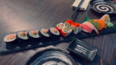 Suşi ve rulo ekmek. Dikdörtgen suşi tabağında suşi ruloları yakın plan. Bir tabak dolusu taze suşi, somon, avokado ve yemek çubuklarıyla servis edilen siyah sushi tohumları. Japon deniz ürünleri 
