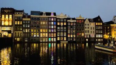 Amsterdam Canal Singel 'da geceleri dans eden evlerle birlikte Hollanda' nın sularındaki aydınlanmanın yansıması. Amsterdam 'ın kanallarında sıra sıra evler. Popüler turistik bölgelerde gece kanalları. Gece görünümü 