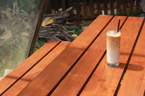 Iced milk coffee with palm sugar and straw on wooden table.