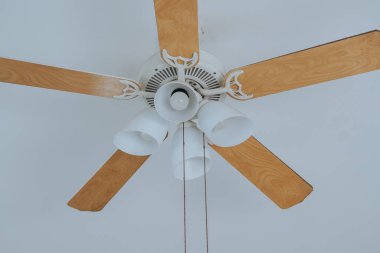 Beyaz tavandan sarkan beş tahta bıçaklı elektrikli lambalar ve tavan vantilatörü. Boşluk resmini kopyala