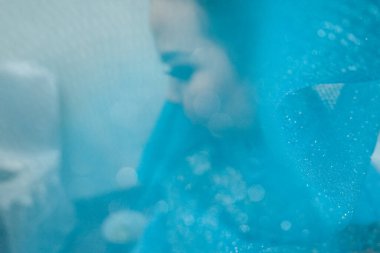 İnce mavi bir kumaşın arkasında bilinmeyen bir kadın, arka planda mavi ışıklı kadın. Soyut duvar kağıdı. Gizemli kadın silueti.