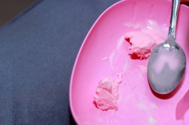 Bir kepçe çilekli dondurma gümüş kaşıkta pembe arka planda dinleniyor.
