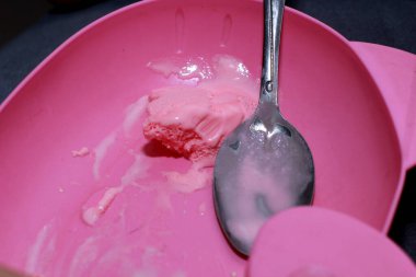 Bir kepçe çilekli dondurma gümüş kaşıkta pembe arka planda dinleniyor.