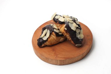 Çikolatalı ve dilimlenmiş bademli kruvasanlar, tahta bir tabakta, beyaz arka planda izole edilmiş.