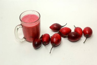 Bir bardakta tamarillo suyu ve yanında da beyaz bir arka planda izole edilmiş tramarillo.