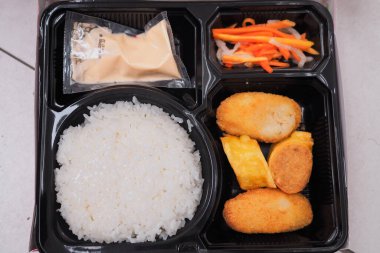 Lezzetli bir Asya bento kutusu. İçinde pirinç, sebze ve çıtır börek var. Öğle ya da akşam yemeği için mükemmel, çeşitli lezzet ve dokuları vurguluyor..