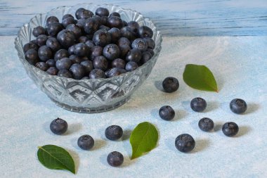Yaban mersinli cam kasede Kanada yaban mersini ve mutfak masasının yanındaki yapraklar. Bir sürü vitamin ve sağlık sigortası olan Kanada yaban mersinli süper yiyecekler. Sağlıklı bir yaban mersini..