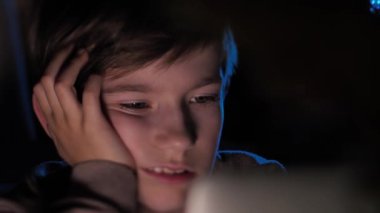 Bir çocuk bir bilgisayarın başında karanlıkta oturur. Karanlıkta ders çalışan bir öğrenci. Küçük bir çocuk tabletten bir video izliyor. Bir çocuk duygusal olarak video izler. Seçici yumuşak odak