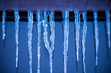 Kışın pencerenin yanındaki buz saçakları. Binanın önü buz saçaklarıyla kaplı. Soğuk havada pencerelerde buz. Buz sarkıtı üzerinde yumuşak bir odak