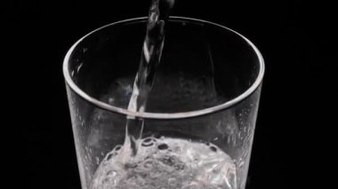 Siyah arka planda bir bardak köpüklü su. Camdan kabarcıklar çıkıyor. Gazlı saf mineralleştirilmiş su.