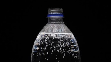 Siyah arka planda karbonatlı su şişesi. Şişeden kabarcıklar çıkıyor. Gazlı saf mineralleştirilmiş su.