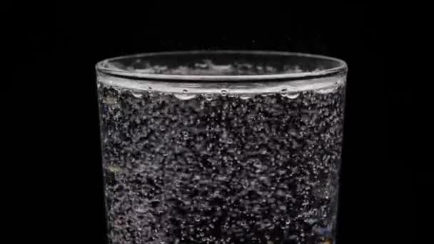 黒い背景に輝く水のガラス 泡がガラスから出てきます 純鉱化ガス水 — ストック動画